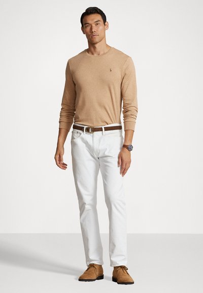 Beige trui met lange mouwen en ronde hals, witte broek, bruine riem en tan schoenen, met een horloge om de linkerpols; effen ontwerp, casual pasvorm.