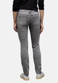 Jeans ajustados de mezclilla gris con cintura alta, detalles de costura visibles, dos bolsillos traseros y un ligero estiramiento. Llevados con zapatillas de color claro.
