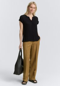 Schwarzes kurzärmliges Oberteil mit V-Ausschnitt, kombiniert mit beigen weiten Hosen. Eine schwarze Ledertasche und flache Sandalen runden das Outfit ab.