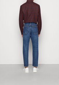 Siniset suoralahkeiset farkut, joissa on kaksi takataskua ja haalistunut pinta. Yhdistetty ruudulliseen, viininpunaiseen paitaan ja valkoisiin tennareihin.