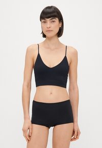 Černý bralet s tenkými nastavitelnými ramínky a V-výstřihem, doplněný o černé vysoké chlapcovské kraťasy, které ladí. Hladká textura.