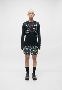 Svart langermet skjorte, shorts med blomstermønster, svart vest med blomsterdekorasjoner og røde snørebånd. Svart sokker og sko fullfører antrekket.