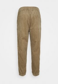 Corduroypantalon in een lichtbruine kleur, met verticale ribbeltextuur, een elastische tailleband en taps toelopende benen die eindigen in strakke manchetten.