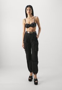 Fekete, flitteres bustier felső vékony pántokkal, fekete cargo nadrággal, amely rugalmas mandzsettákkal és arany Moschino övvel párosítva. Fekete platform magassarkúk.