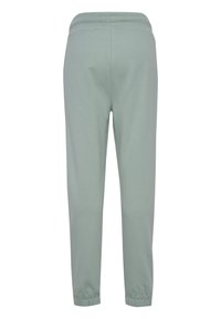 Lichtgroene broek met elastische taille en elastische boorden, gezien van de achterkant tegen een witte achtergrond.
