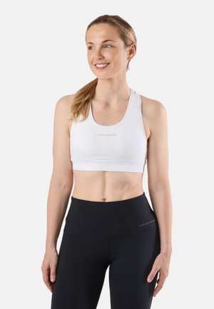 Brassière de sport blanche à fines bretelles avec un logo, associée à un legging noir taille haute. Texture lisse, coupe ajustée et style minimaliste.