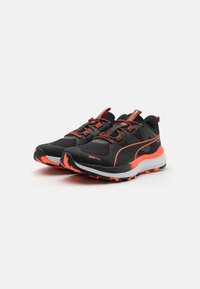 Baskets de sport noires avec des accents orange ; tige en maille texturée, col rembourré et semelle robuste pour une meilleure adhérence. Conception légère et respirante.