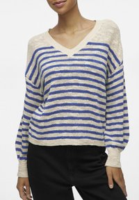 Pull en tricot avec un col en V, présentant des rayures horizontales bleues et crème, des manches longues et une coupe loose, en tissu texturé, avec des poignets côtelés.