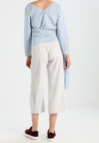 Haut portefeuille rayé bleu à manches longues, associé à un pantalon court gris clair et des baskets bordeaux. Tissu lisse avec une coupe décontractée.