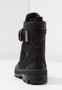 Černé kotníkové boty vyrobené z texturované tkaniny a syntetického materiálu. Disponují páskem s přezkou a robustní gumovou podrážkou s výrazným vzorem.