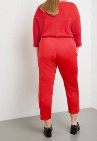 Haut tricoté rouge à manches trois-quarts associé à un pantalon rouge taille haute, fuselé, en tissu lisse et texture élégante.