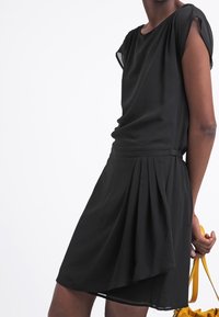 Robe noire courte avec une coupe décontractée, dotée d'une taille cintrée, de détails drapés et de manches légèrement translucides. Tissu lisse et fluide.