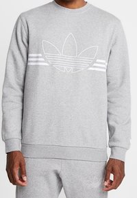 Grå sweatshirt gjord av ett bomullsliknande material, med en stor vit logotyp och tre horisontella vita ränder på framsidan. Klassisk crewneck-design.