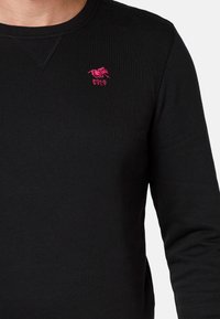 Czarny długi rękaw sz sweatshirt z bawełny, z okrągłym dekoltem i małym różowym haftowanym logo na piersi.