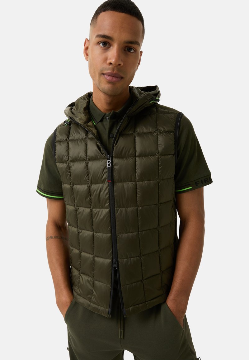 Olivengrüne gepolsterte Weste mit Reißverschluss, Kapuze und gestepptem Muster. Getragen über einem dunkelgrünen Polo mit grünen Akzenten.