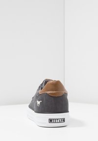 Šedé plátěné tenisky s hnědým koženým akcentem na patě, bílou gumovou podrážkou a malým logem koně na boku. Nízký design.