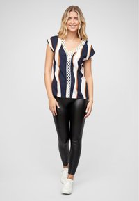Chemisier à rayures bleu marine et blanches avec des accents orange, décolleté en V et bordure en dentelle. Associé à un legging noir et des baskets blanches.