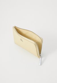 Portefeuille en cuir jaune avec fermeture éclair, featuring un logo argenté et une texture lisse. L'intérieur est beige avec une doublure simple.
