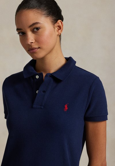 Mörkblå pikétröja med texturerat tyg, utrustad med en treknappsklaff och en liten röd broderad logotyp på vänster bröst.