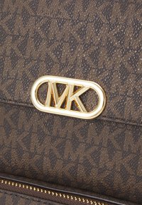 Pruun mustriga käekott, millel on tekstureeritud kangas, kuldne logo riistvara ja tõmbluku detail, disainitud struktureeritud kujuga.