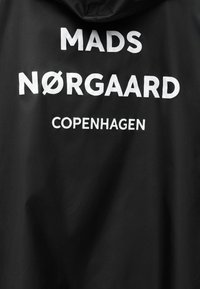 Μαύρο ύφασμα με λευκό κείμενο που γράφει «MADS NØRGAARD COPENHAGEN» με έντονα κεφαλαία γράμματα.