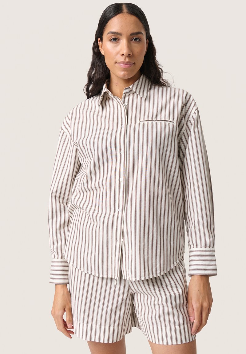 Set di camicia a righe e pantaloni corti in beige e marrone. Camicia con bottoni presenta una tasca sul petto e maniche lunghe. Tessuto leggero e texture.