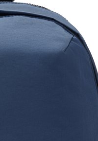 Blue nylon backpack with smooth texture, rounded shape, subtle stitching, and a zip closure. No visible patterns or hardware details.
