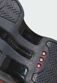 Black sneaker sole features a textured rubber with zigzag pattern, glossy accents, and three red circular elements near the heel.