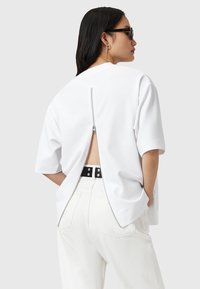 Witte oversized T-shirt met korte mouwen, met een ritssluiting aan de achterkant. Gemaakt met lichtgekleurde broek en een zwarte riem.