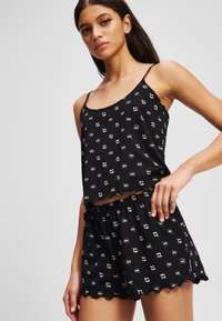 Conjunto de pijama negro que incluye una camiseta de tirantes corta y pantalones cortos, ambos con un patrón divertido, bordes ondulados y cinturilla elástica.