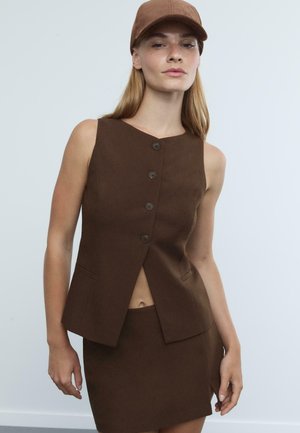 Hnědý bezrukávový blazer s V-výstřihem, pěti knoflíky a bočními kapsami, doplněný o odpovídající mini sukni s mírným rozparkem.
