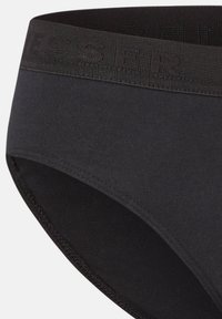 Shorty en coton noir avec une large ceinture élastique affichant un logo texturé. Texture lisse et détails de couture minimalistes.