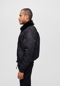 Chaqueta bomber negra con collar de pelo sintético, cierre de cremallera en la parte delantera, bolsillos laterales y puños acanalados. Material texturizado con un acabado suave.