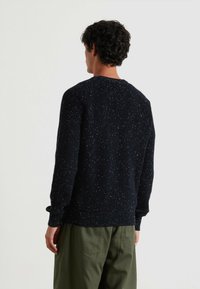 Suéter de punto azul marino con un patrón texturizado y motas, que presenta mangas largas, puños acanalados y un cuello redondo. Combinado con pantalones verdes.