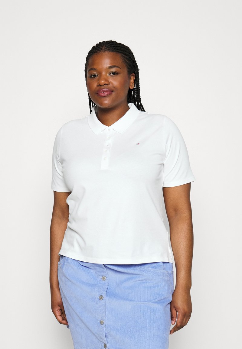 Polo blanco de manga corta, con cuello y botonera en la parte frontal. Presenta un pequeño logo en el lado izquierdo del pecho. Combinado con una falda azul claro.