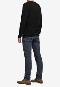 Svart långärmad skjorta, mörkblå jeans och bruna ankelstövlar. Skjortan har en rund hals och en avslappnad passform; jeansen är raka.