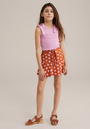 Top senza maniche di colore rosa con spalline arricciate, abbinato a una gonna arancione a fantasia con disegni di fiori bianchi. Zoccoli marroni completano l'outfit.