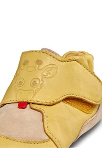 Chaussure bébé en cuir jaune avec un motif de visage de girafe, petit détail de langue rouge, côté découpé et coutures apparentes sur le dessus.