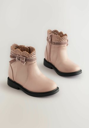 Botas de tobillo de cuero rosa con bordes ondulados, un lazo decorativo de terciopelo y una cremallera lateral. Las suelas de goma negra proporcionan estabilidad.