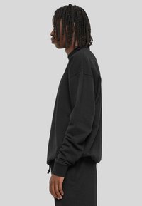 Sweatshirt noir en coton avec des manches longues, des poignets côtelés et une coupe décontractée. Stylé avec un col rond et des détails minimalistes.