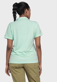 Polohemd in mintgrün mit weicher Textur, kurzen Ärmeln und klassischem Kragen. Kombiniert mit olivgrünen Hosen mit Gesäßtaschen.