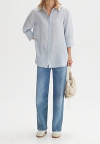 Ljusblå linneskjorta med knappar och långa ärmar, tillsammans med löst sittande ljusa jeans och en beige dragsko-väska. Sneakers fulländar looken.