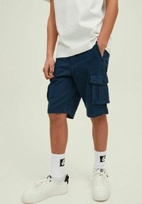Shorts cargo blu navy con tasche laterali, dettagli con bottoni e una vestibilità comoda, abbinati a sneakers bianche e calzini con logo.