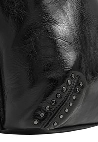 Primer plano de una superficie de cuero negro con textura visible y pequeños clavos metálicos redondos dispuestos en dos líneas sobre un detalle cosido.