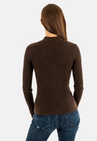 Maglia a maniche lunghe marrone a costine con colletto alto, design aderente e texture morbida, abbinata a jeans fitted blu scuro.