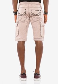Beige Cargo-Shorts mit kontrastierenden Nähten, ausgestattet mit zwei Gesäßtaschen und einer seitlichen Cargo-Tasche. Getragen mit dunklen Sneakers.