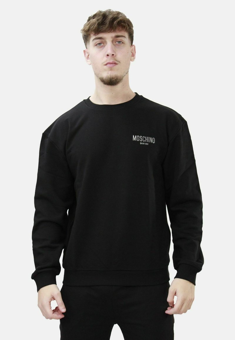 Felpa nera in cotone, con colletto rotondo e maniche lunghe. Davanti presenta la scritta "MOSCHINO SWIM" in bianco. Design semplice.