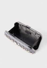 Mała otwarta srebrna kopertówka z czarnym satynowym wnętrzem i ozdobą z klejnotów wzdłuż przedniej krawędzi na białym tle.