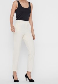 Krämfärgade skräddarsydda byxor med rak benform, uppvikta fållar och en mjuk textur. Kombineras med en svart åtsittande linne och klackar.