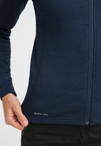 Navy quick-dry long-sleeve top with textured fabric and full zip. Features a label at the hem reading "QUICK DRY." Form-fitting design.